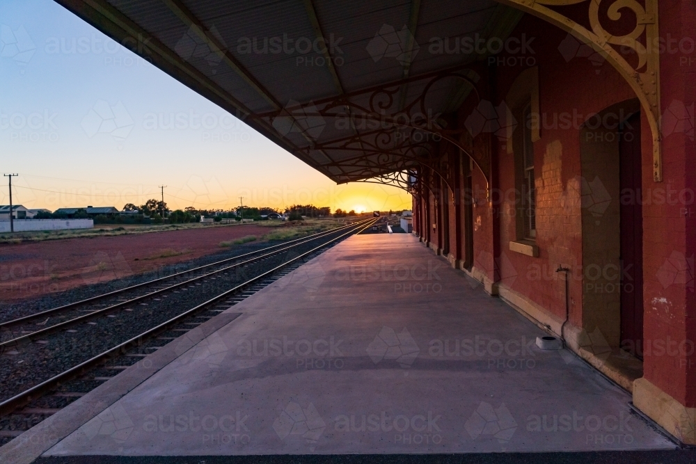 Looking along a deserted railway station platform at a distance sunrise - Australian Stock Image