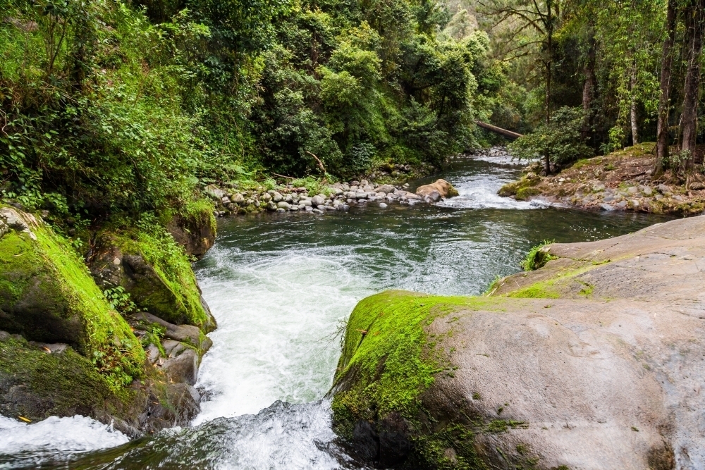 Looking along Allyn River at mossy green rocks and bubbling waterfall - Australian Stock Image