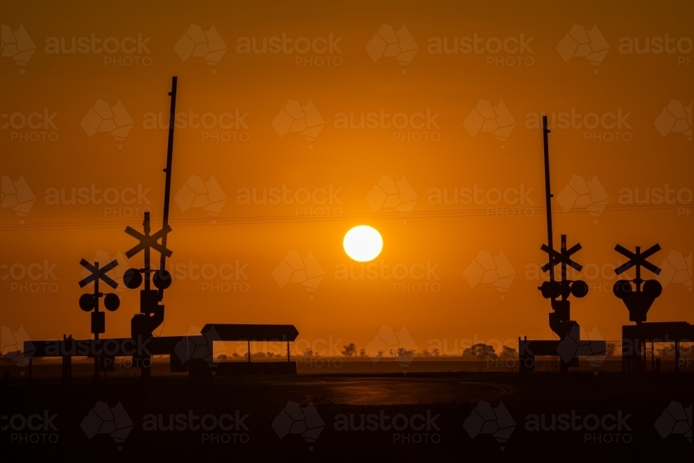 Looking at the sun rising directly behind a railway line crossing. - Australian Stock Image