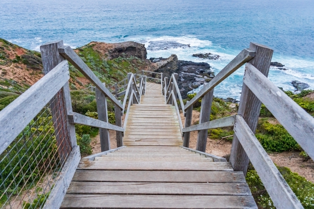 Looking down a long wooden staircase towards a rocky coastline - Australian Stock Image