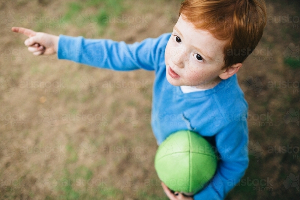 Looking down at a young boy holding a football and pointing - Australian Stock Image