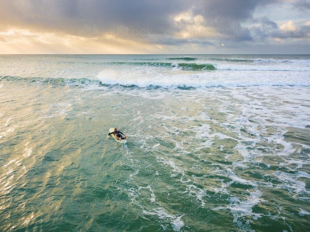 Looking down on a lone surfer paddling into waves under a darkening sky - Australian Stock Image