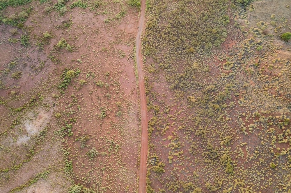 Looking down on a red earth dirt track speckled with green bushes over the land. - Australian Stock Image
