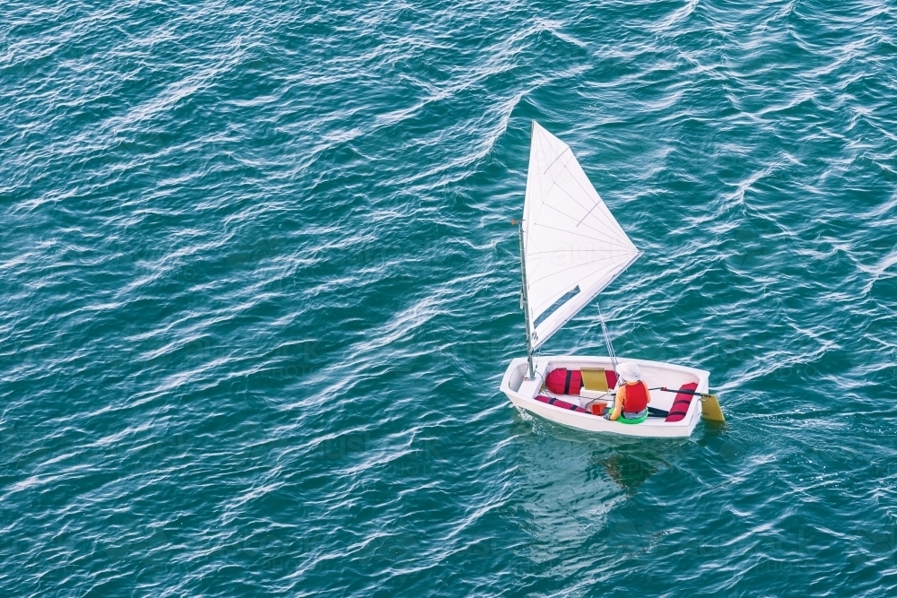 Looking down on a sailor in a small boat on a blue sea - Australian Stock Image