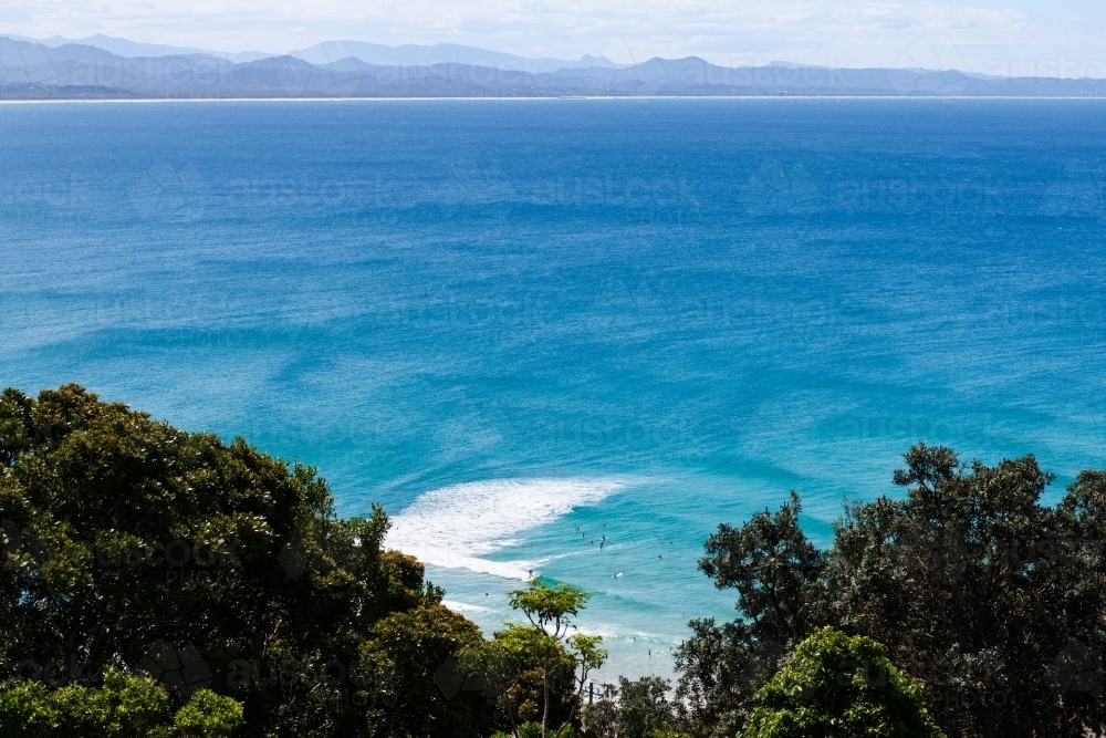 Looking down on surfers in blue ocean with patterns in water and distant mountains - Australian Stock Image