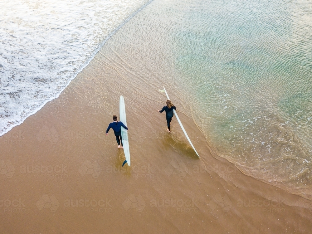 Looking down on two surfers walking on a beach between waves - Australian Stock Image