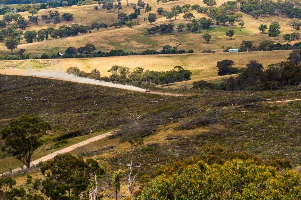 Looking on a distant rally car speeding along a country road with dust trailing behind - Australian Stock Image