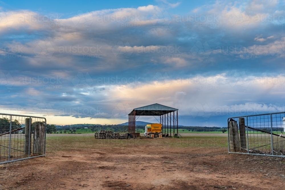 Looking through a gateway at farm machinery and trucks in a shed in the middle of a paddock - Australian Stock Image