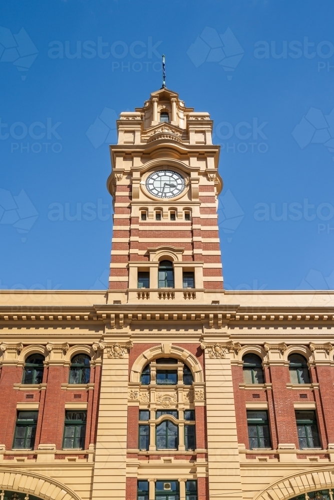 Looking up at a tall clock tower with intricate brickwork against a blue sky - Australian Stock Image