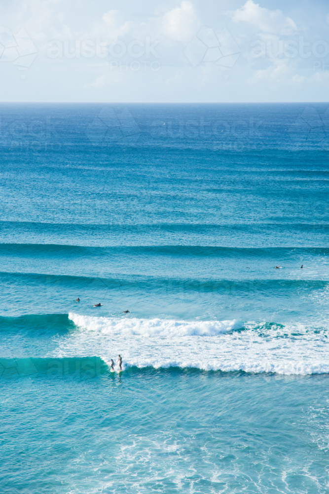 Lots of blue waves rolling in with people surfing at Byron Bay - Australian Stock Image