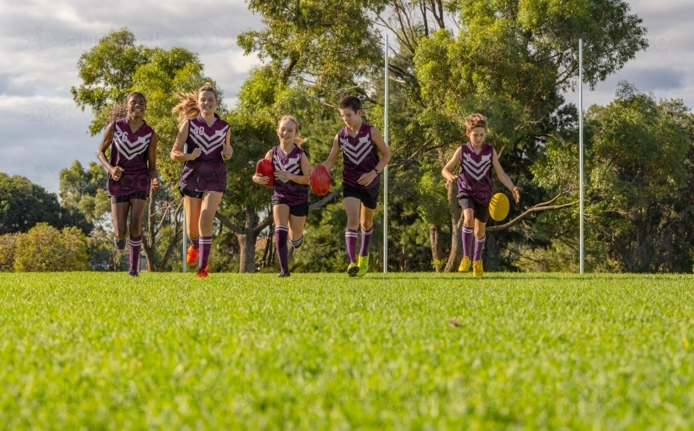 low angle image of children running on grass with afl footballs - Australian Stock Image