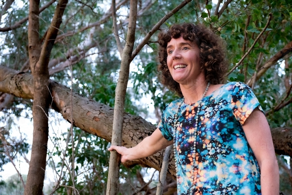 Low angle of Mature woman holding onto trunk of tree looking out - Australian Stock Image