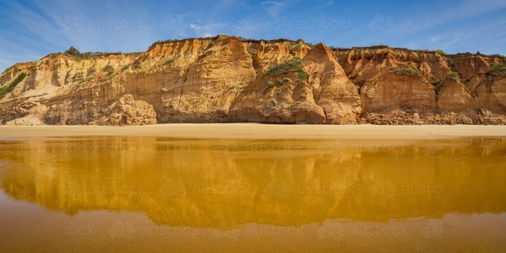 Low angled view of coastal sea cliffs reflected in wet sand on the beach below - Australian Stock Image