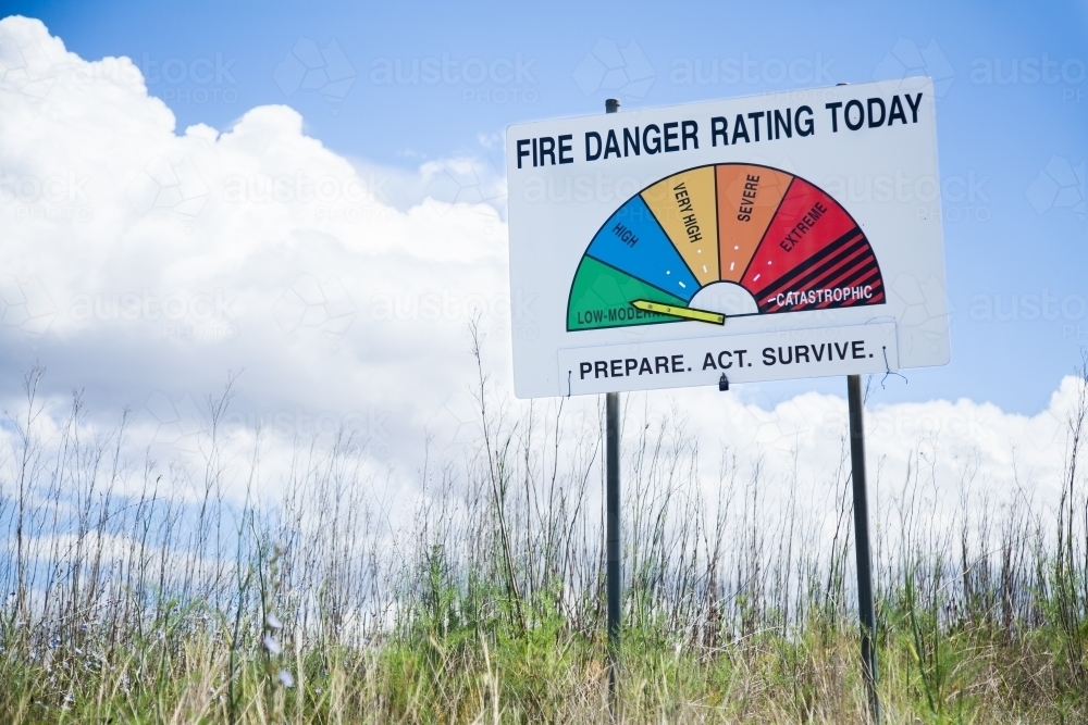 Low moderate fire danger rating on sign in long grass - Australian Stock Image