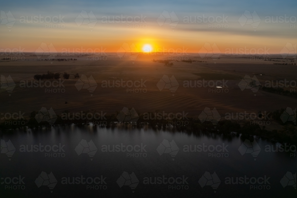 Low sun over landscape with lake in foreground - Australian Stock Image