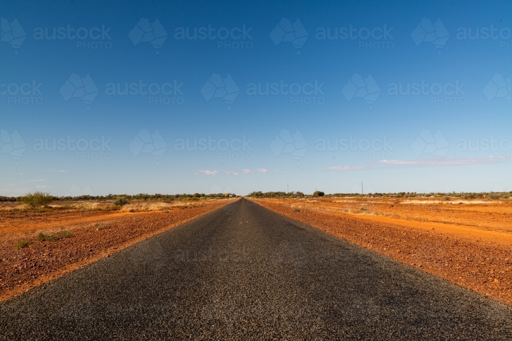 Low, wide view of bitumen road in desert country, converging at  horizon with clear blue sky - Australian Stock Image