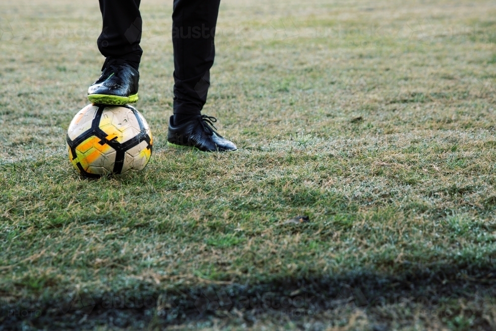 Lower body extremity shot of a man standing on the field stepping on a soccer ball with one foot - Australian Stock Image