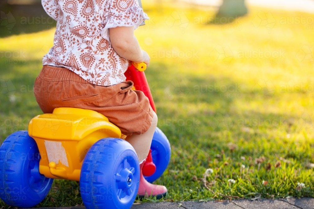 Lower body shot of toddler riding tricycle on lawn grass - Australian Stock Image