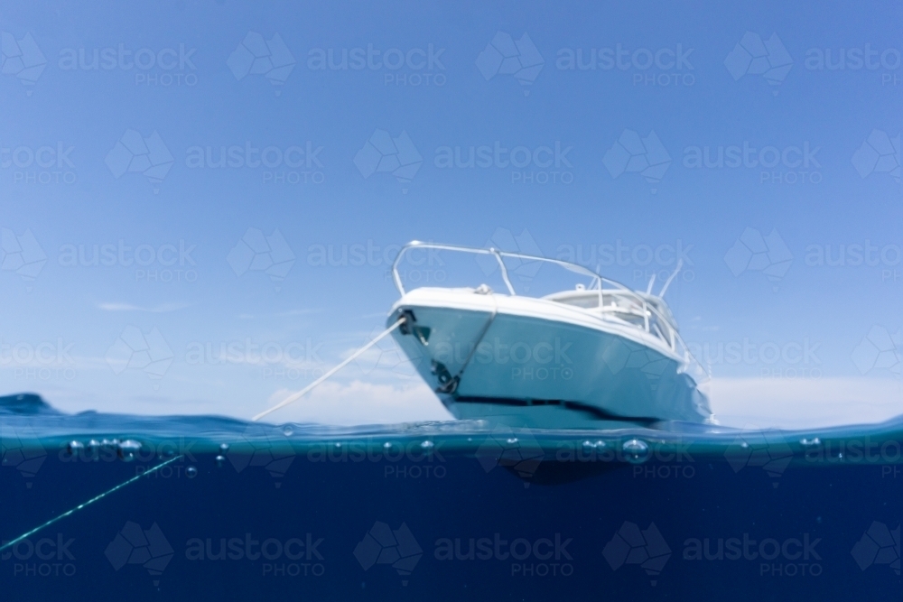 Luxury boat sitting on anchor floating in deep blue water with blue sunny skies in background - Australian Stock Image