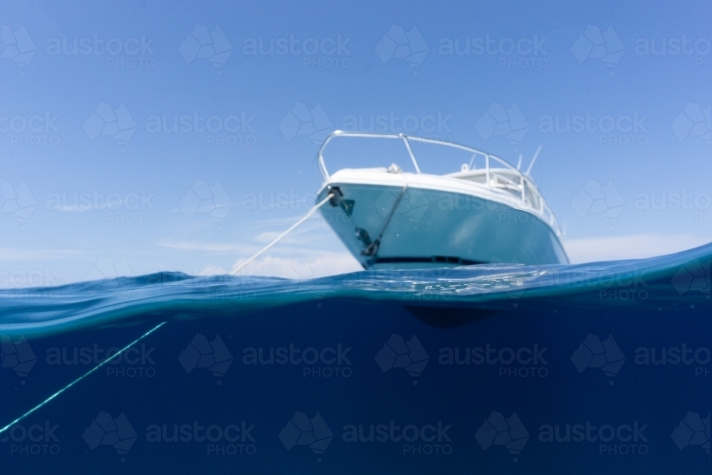 Luxury boat sitting on anchor floating in deep blue water with blue sunny skies in background - Australian Stock Image