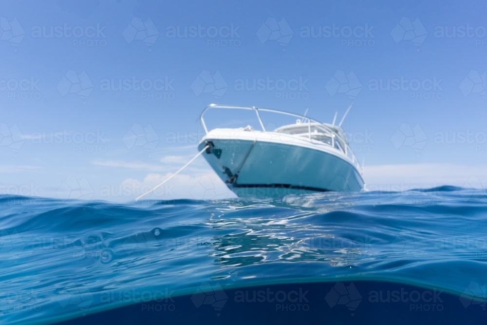 Luxury boat sitting on anchor floating in deep blue water with blue sunny skies in background - Australian Stock Image