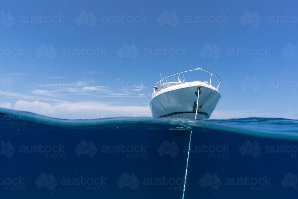 Luxury boat sitting on anchor floating in deep blue water with blue sunny skies in background - Australian Stock Image