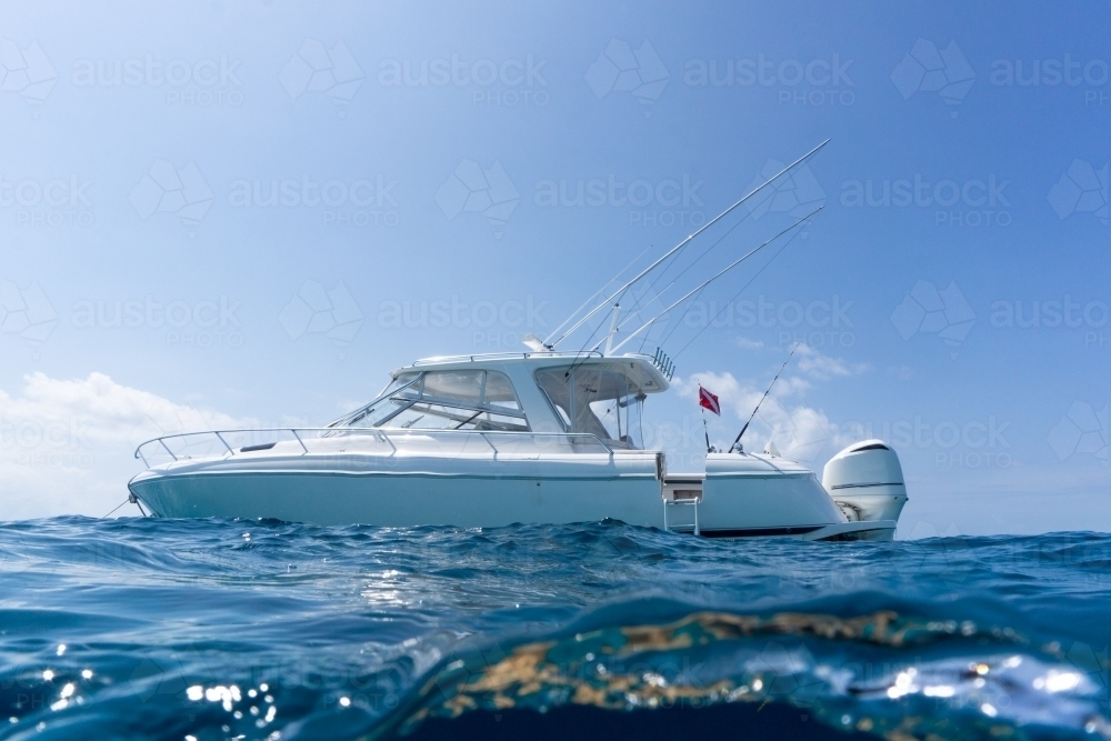 Luxury boat with dive flag, floating in deep blue water with blue sunny skies in background - Australian Stock Image