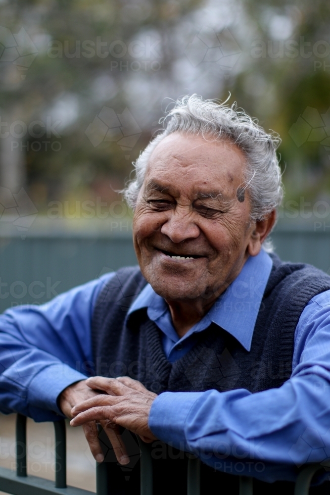 Male Aboriginal elder smiling and leaning against fence - Australian Stock Image