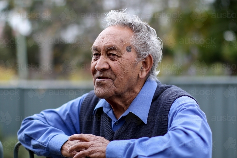 Male Aboriginal elder smiling and leaning against fence - Australian Stock Image