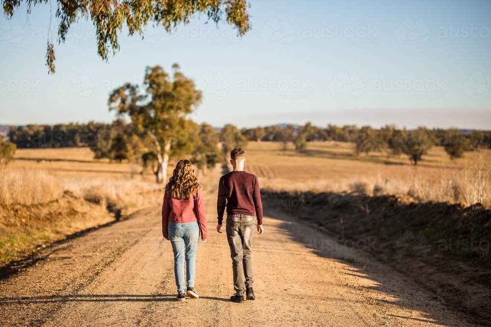 Male and female walking on dirt road in country in afternoon light - Australian Stock Image