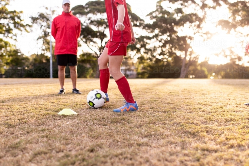 Male coach standing and teaching tween girls as they train for football - Australian Stock Image