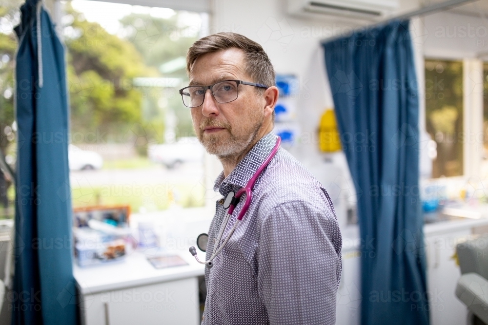 Male doctor wearing stethoscope around his neck looking at camera in the clinic - Australian Stock Image