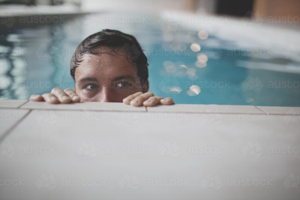 Male swimmer peeking over the edge of contemporary indoor lap pool - Australian Stock Image