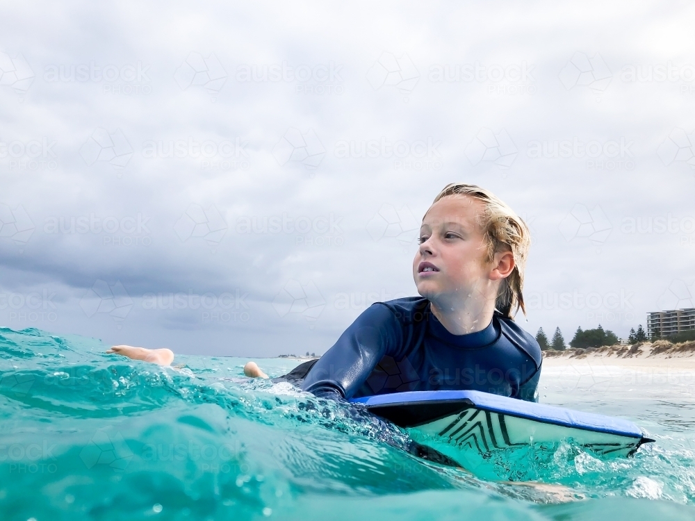 Male youth paddling boogie board in ocean on overcast day - Australian Stock Image