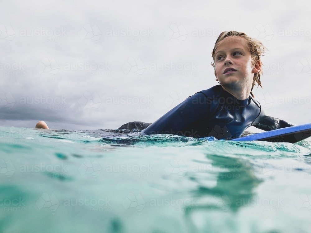 Male youth paddling boogie board in ocean on overcast day - Australian Stock Image