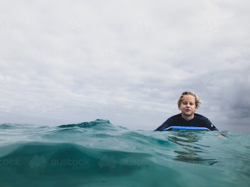 Male youth paddling boogie board in ocean on overcast day - Australian Stock Image