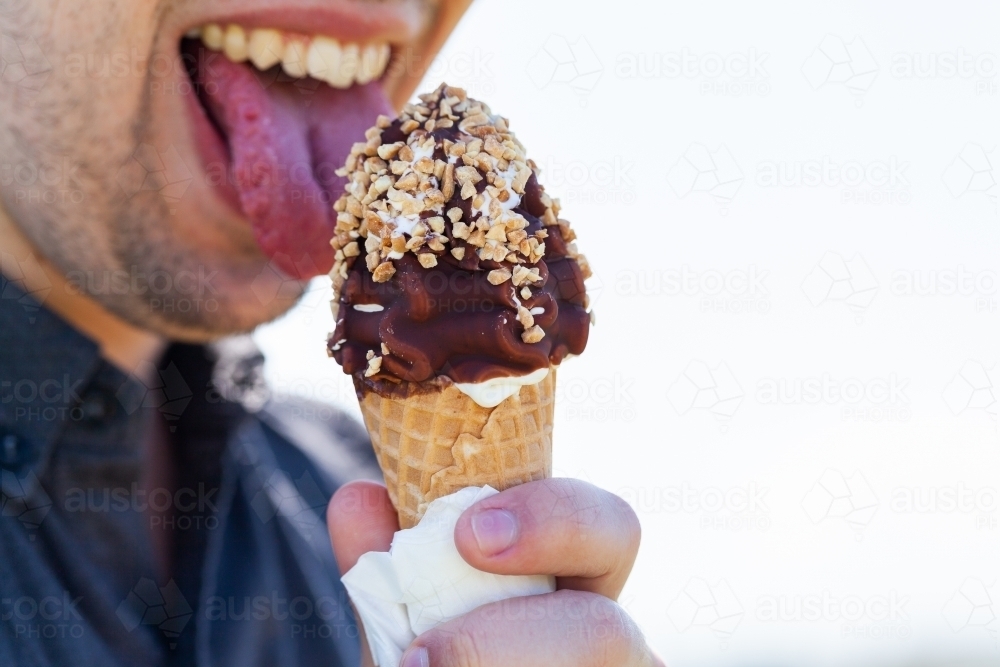 man about to eat soft serve ice cream with choc nut toping on sunny day - Australian Stock Image