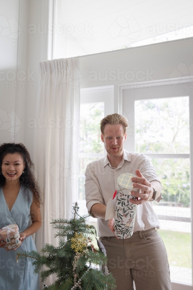 Man and woman holding presents next to Christmas tree - Australian Stock Image