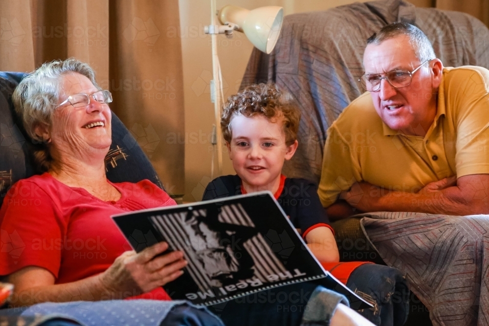 Man and woman laughing with young child on lounge in house - Australian Stock Image