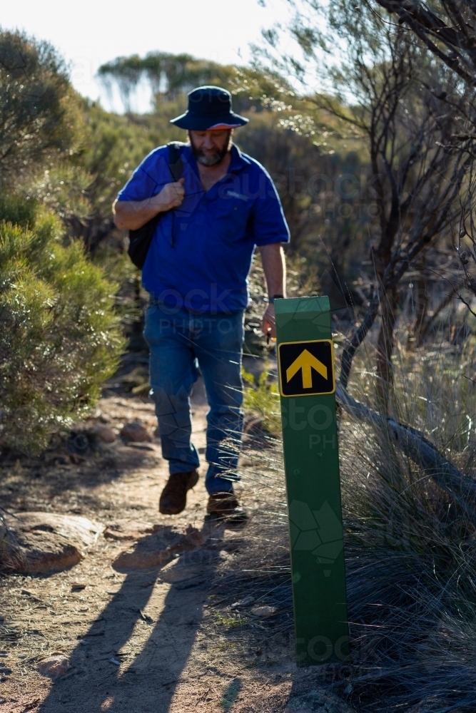 man backlit on walking trail with directional sign post - Australian Stock Image