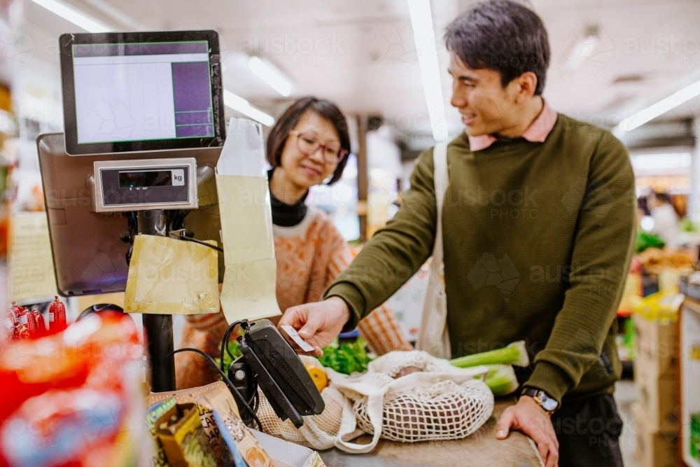 Man buying fresh produce from woman at supermarket counter - Australian Stock Image