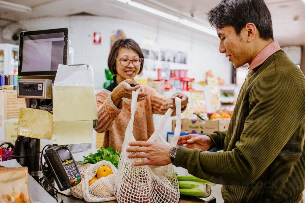 Man buying fresh produce from woman at supermarket counter - Australian Stock Image