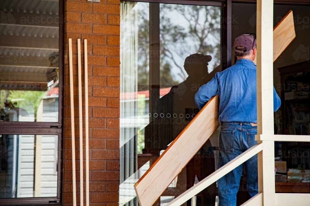 Man carrying plank of timber into house - Australian Stock Image