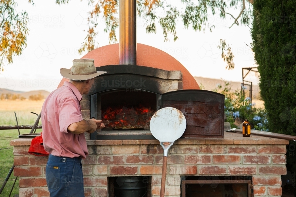 Man cooking home made pizza in outdoor pizza oven - Australian Stock Image