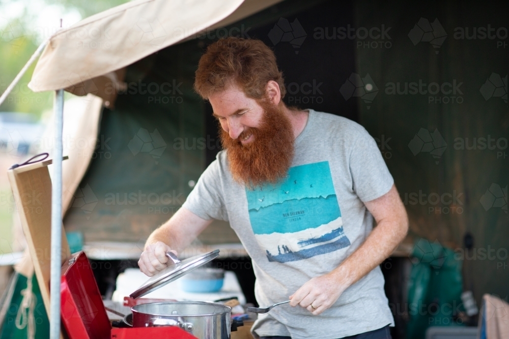 Man cooking on camp stove in camper trailer - Australian Stock Image