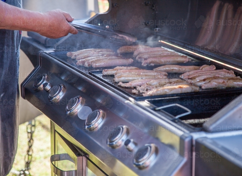 Man cooking snags for dinner on a BBQ - Australian Stock Image