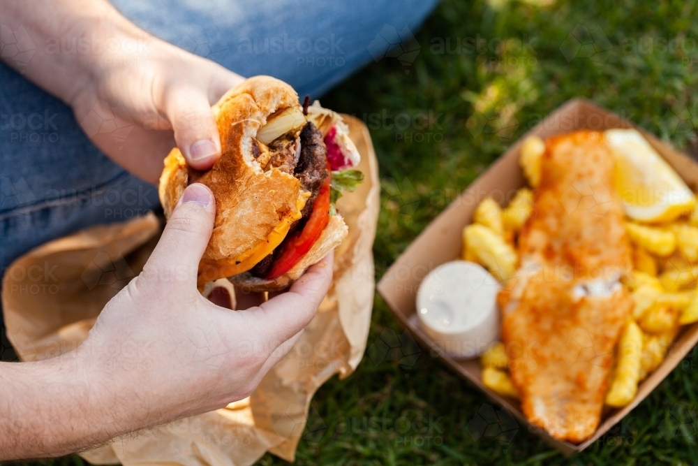 man eating burger with fish and chips outside in park - Australian Stock Image