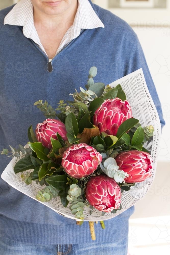 Man holding a bunch of pink flowers and leaves wrapped in paper - Australian Stock Image