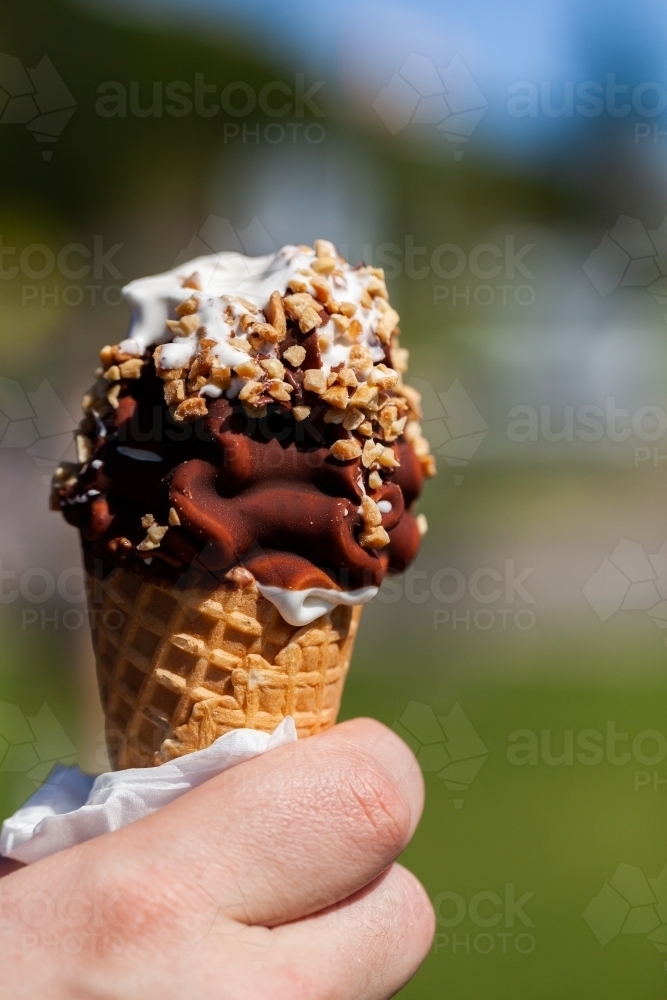 man holding half eaten soft serve ice cream with choc nut toping on sunny day - Australian Stock Image