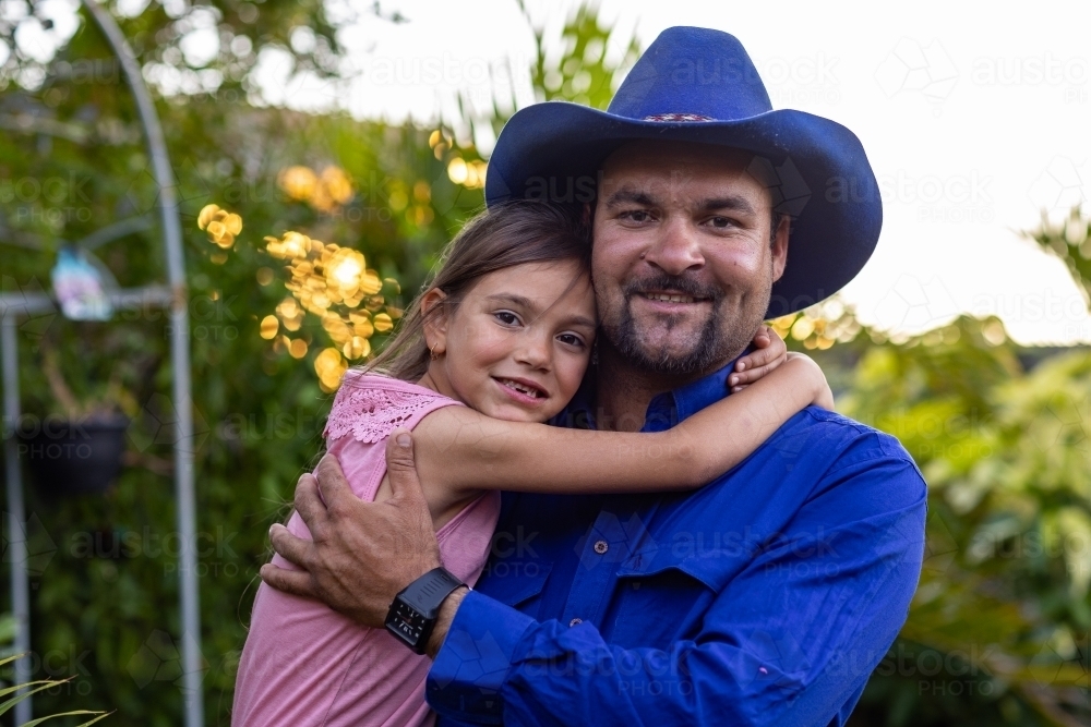 man holding his little girl who is hugging him around the neck - Australian Stock Image